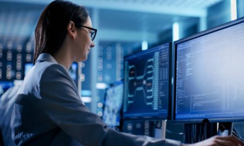 Close-up Shot of Female IT Engineer Working in Monitoring Room. She Works with Multiple Displays.
